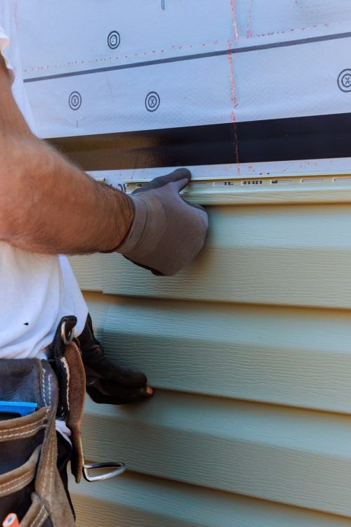 Handyman process installing vinyl PVC siding during construction on a facade new home
